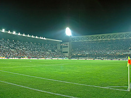 Ein beleuchtetes Fußballstadion mit vollen Zuschauerrängen und leerem Spielfeld bei Nacht