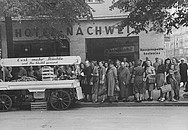 Historisches Foto zeigt viele Frauen mit Einkaufstaschen vor einem Früchtewagen.
