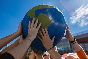 Mehrere nach oben gestreckte Hände halten einen Globus
