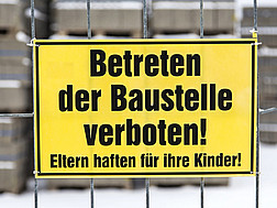 Ein gelbes Schild an einem Baustellenzaun mit der Aufschrift "Betreten der Baustelle verboten! Eltern haften für ihre Kinder!"
