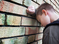 Ein Junge lehnt sich gegen eine Ziegelmauer und lehnt die Stirn an seinen rechten Unterarm.