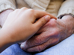 Eine junge Hand hält Hände eines älteren Menschen.