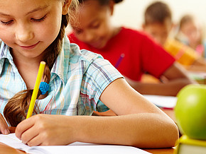 Ein Mädchen sitzt in der Schulbank und schreibt