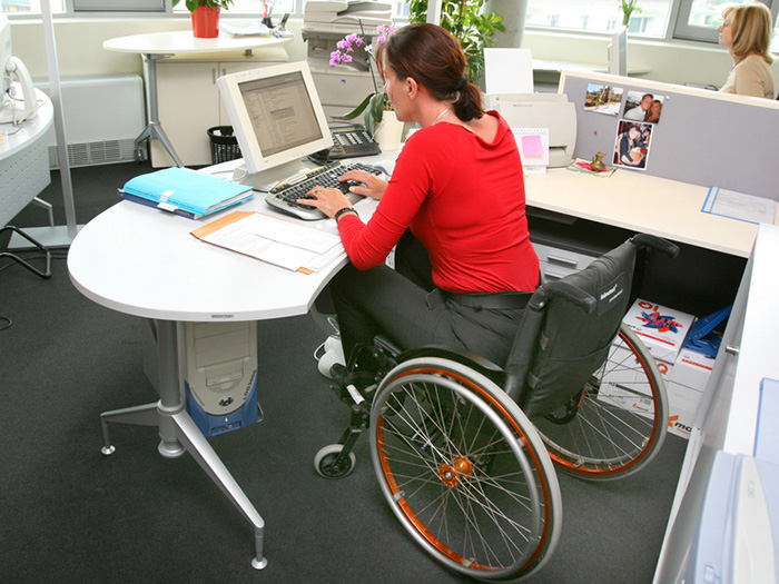 Eine Frau im Rollstuhl im Büro am Arbeitsplatz mit Computer